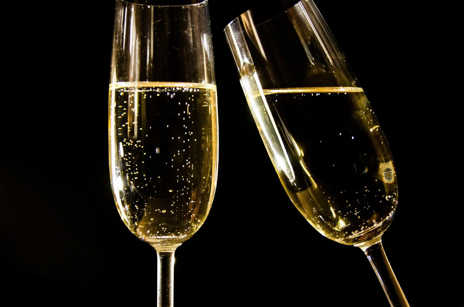 Close-up of champagne glasses with bubbles against a black background, perfect for celebrations.